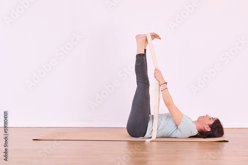 The pose being executed by a young woman, who is using a strap to stretch her foot during her yoga practice. photo