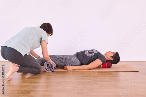 A yoga class with a teacher placing props under the body to correct posture