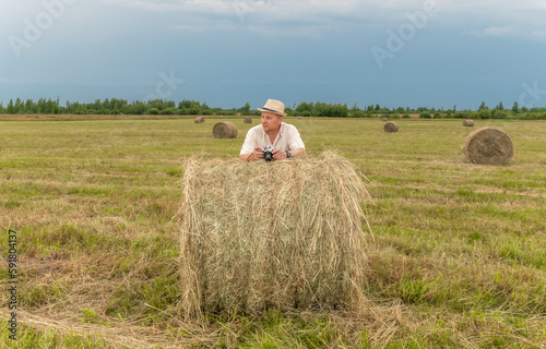 A man sitting on a large armful of straw in an empty field. Against the blue sky.