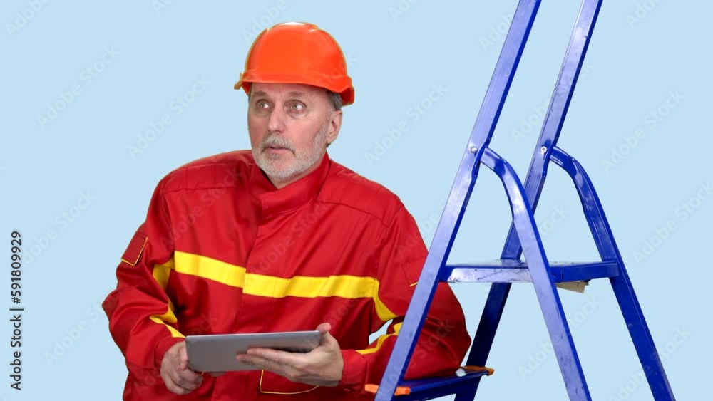 Senior aged upset worker with tablet device leans on a blue ladder. Isolated on blue background. Senior aged upset worker with tablet device leans on a blue ladder. Isolated on blue background.