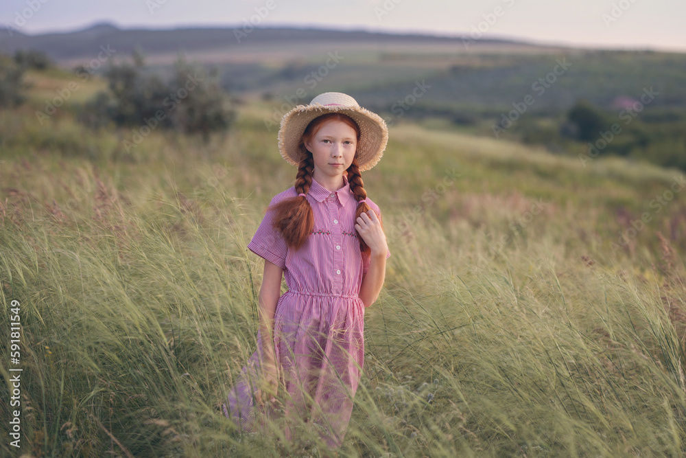 Red-haired girl in a hat at sunset on a meadow