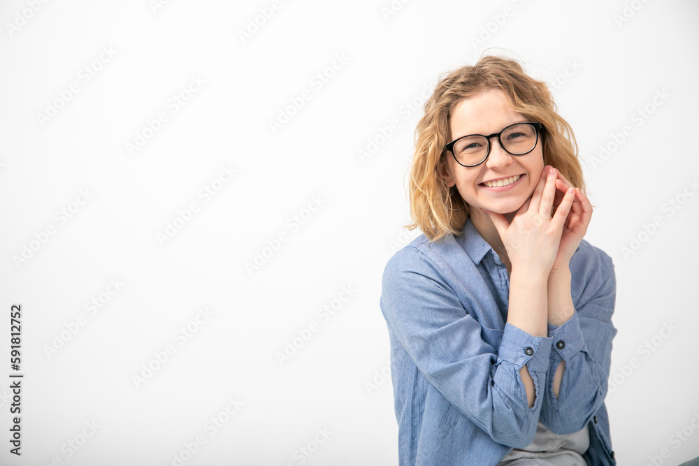 Portrait of young joyous attractive woman sit looking at camera, folding hands near face on white background. Emotions. Portrait of young joyous attractive woman sit looking at camera, folding hands near face on white background. Emotions.
