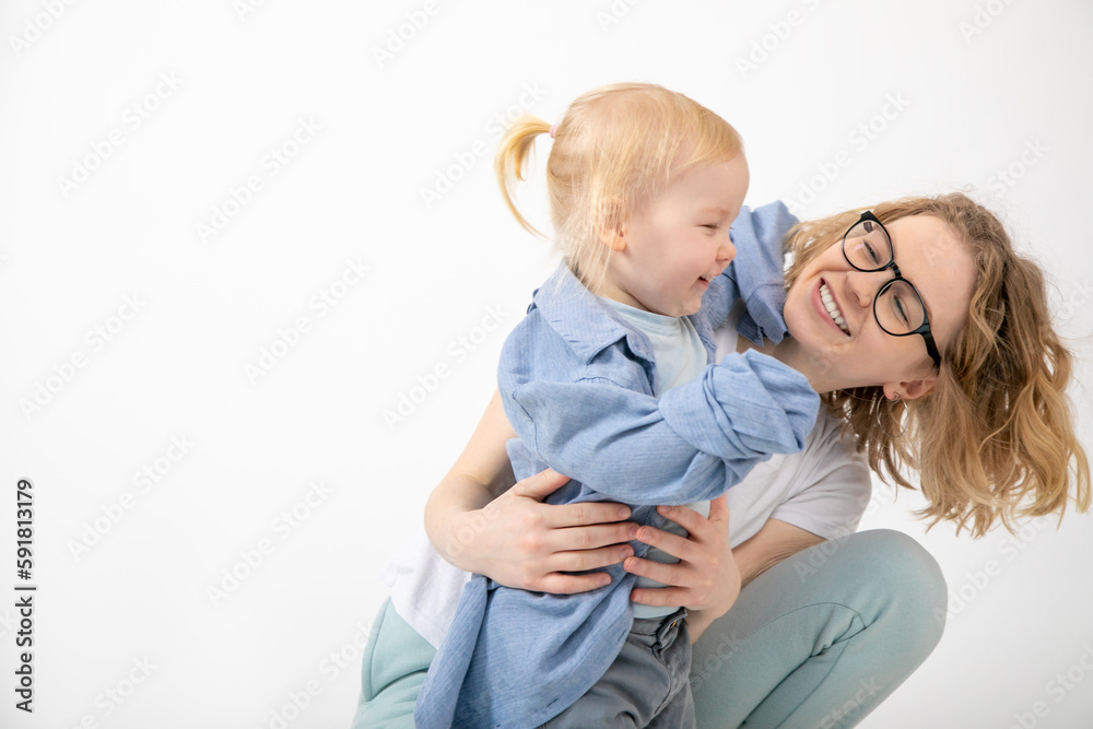 Young woman mother holding catching looking at lovely little blond girl baby daughter wearing oversized denim shirt. Young woman mother holding catching looking at lovely little blond girl baby daughter wearing oversized denim shirt.