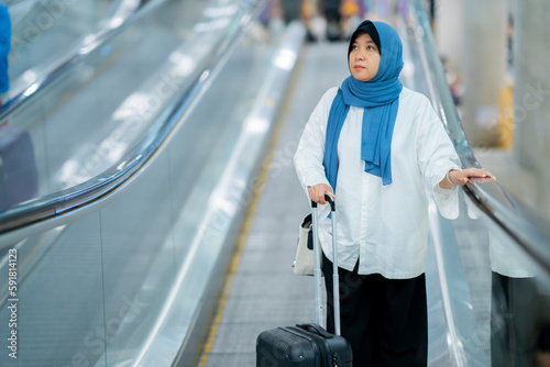 An Asian Muslim wearing a blue hijab is preparing for a vacation and she is at the airport. She is waiting for her friends, Muslim travelers.