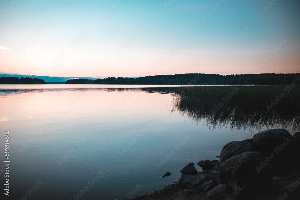 Scenic view of a tranquil lake reflecting a rocky shore covered with plants at sunset