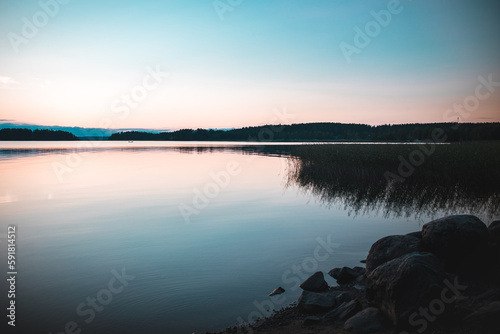 Scenic view of a tranquil lake reflecting a rocky shore covered with plants at sunset