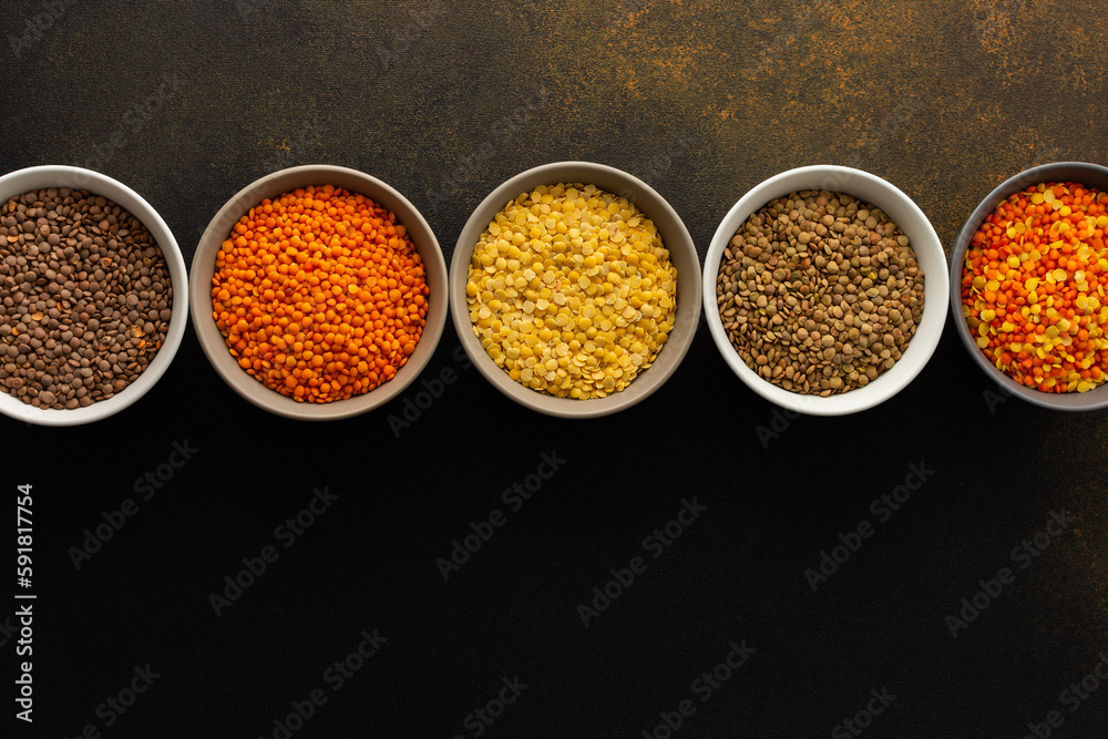 Multicolored lentils in bowls on a brown background, yellow and brown, green and orange lentils, healthy legumes, top view, copy space