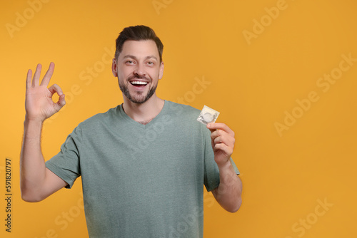 Happy man with condom showing ok gesture on orange background. Space for text