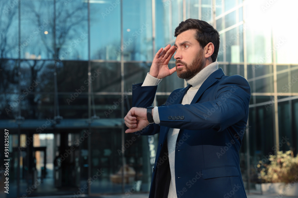 Businessman checking time on watch near building. Being late concept Businessman checking time on watch near building. Being late concept