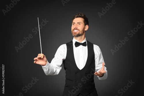 Happy professional conductor with baton on black background