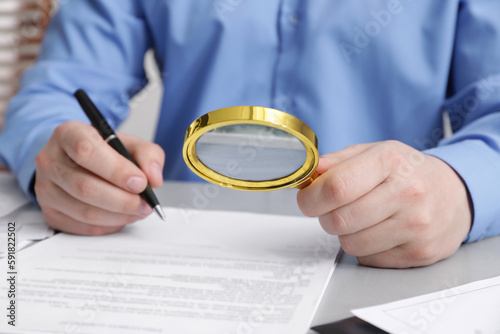 Man looking at document through magnifier at white table, closeup. Searching concept