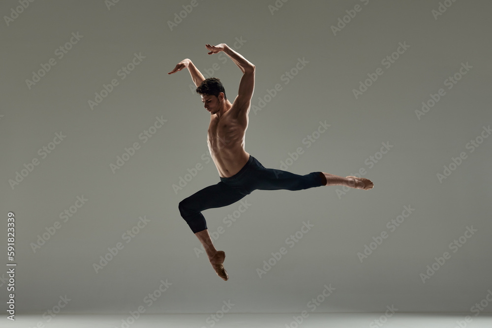 Young handsome man with muscular shirtless body, ballet dancer making performance over grey studio background. Concept of art, classical dance, inspiration, creativity, fashion, beauty, choreography