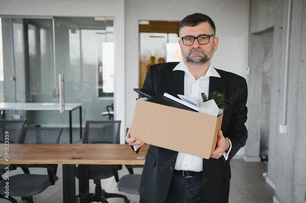 Portrait of sad dismissed senior old business man worker taking his office supplies in the box. Pensioner mature retire from work carry staff back home. Lifestyle business retirement, quit job concept Portrait of sad dismissed senior old business man worker taking his office supplies in the box. Pensioner mature retire from work carry staff back home. Lifestyle business retirement, quit job concept