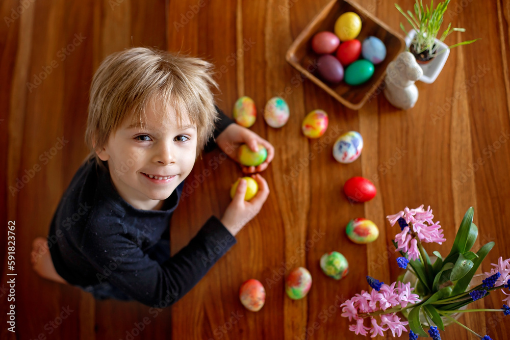 Fototapeta premium Little blond toddler boy child coloring easter eggs at home, Czech Republic tradition