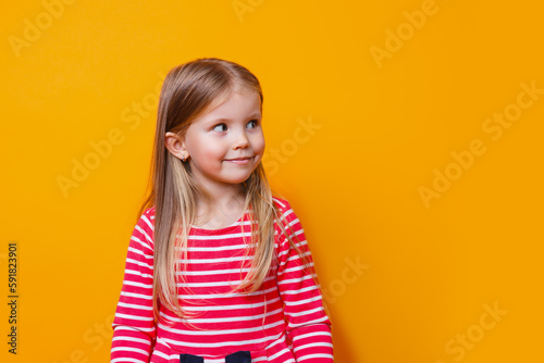 Closeup portrait of adorablel kid in red dress looking away with happy carefree smile on yellow studio backgrouind photo