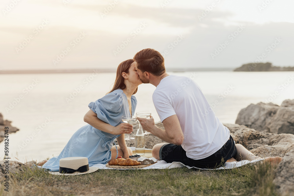 Fototapeta premium Romantic picnic of couple in love on beach at sunset. They kissing and feeling love. The concept of leisure, privacy, communication and vacation. Copy space.