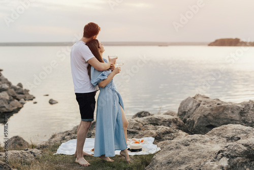 Boyfriend and girlfriend holding wine glasses with beverage and standing on the beach at sunset.