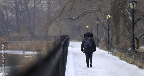 Slow motion shot of a Woman walking by Central Park's Jacque Onassis Reservoir as snow falls photo