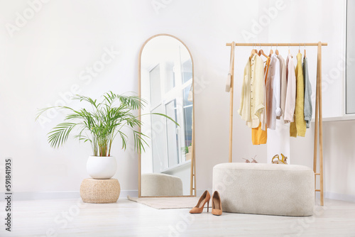 Stylish dressing room interior with mirror, ottoman and clothing rack