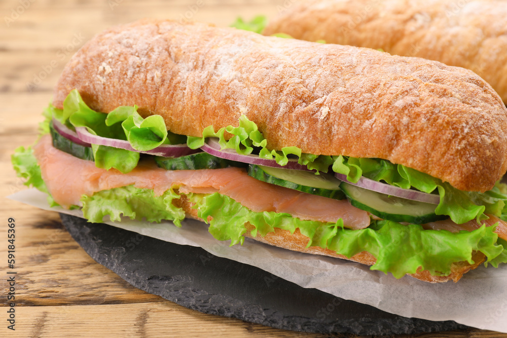 Delicious sandwich with fresh vegetables and salmon on wooden table, closeup