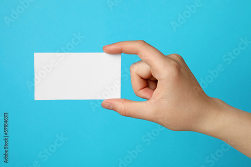 Woman holding blank gift card on light blue background, closeup