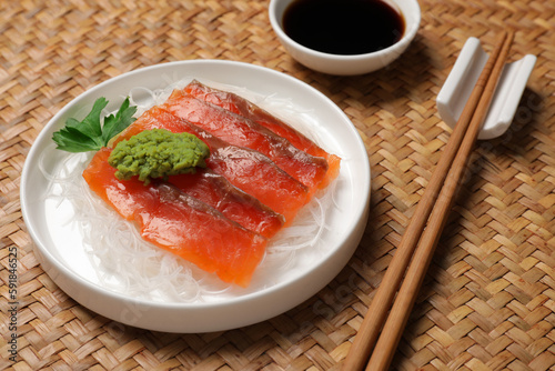 Sashimi set (raw salmon slices) served with funchosa, parsley, vasabi and soy sauce on wicker surface