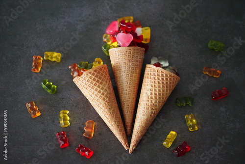 Colorful gummy bears and the hearts by the waffle cones on a black surface