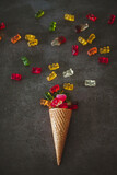 Vertical closeup of an ice cream cone with gummy bears and heart jellies on the dark surface