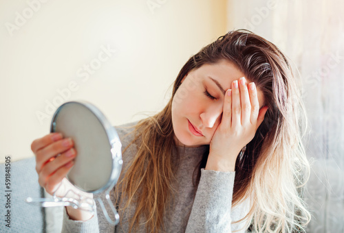 Stressed woman is sad about dirty oily and greasy hair looking in mirror at home. Healthcare. Hormonal imbalance
