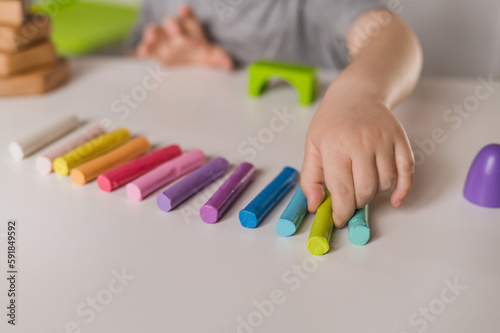 little boy three years old sits at table with colored crayons and plasticine and plays sensory educational games. Closeup of hands focus on colored plasticine and constructor. Unrecognizable no face
