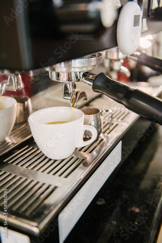 In the white cup that is in the coffee machine, fresh coffee with foam flows out of the holder