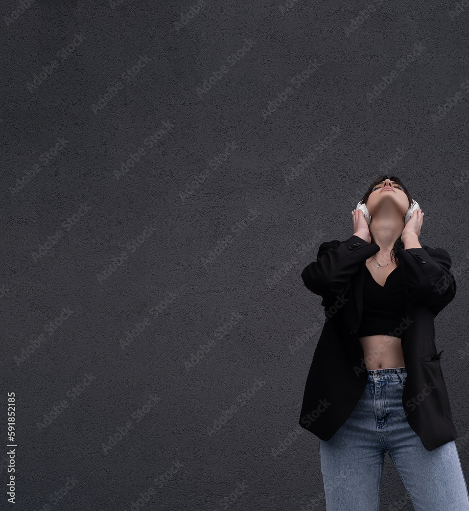 Carefree attractive brunette girl, dressed in a gray sweater, listening to music on headphones, standing on a gray background Carefree attractive brunette girl, dressed in a gray sweater, listening to music on headphones, standing on a gray background
