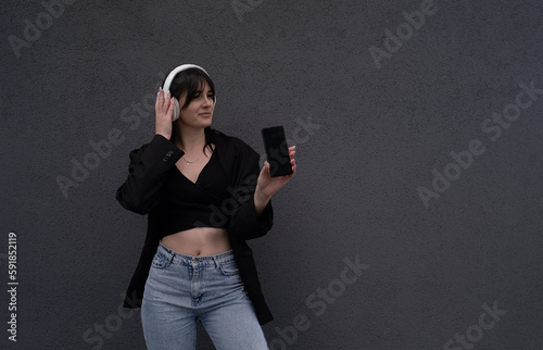 a teenager shows a smartphone, she listens to music in headphones isolated on a gray background
