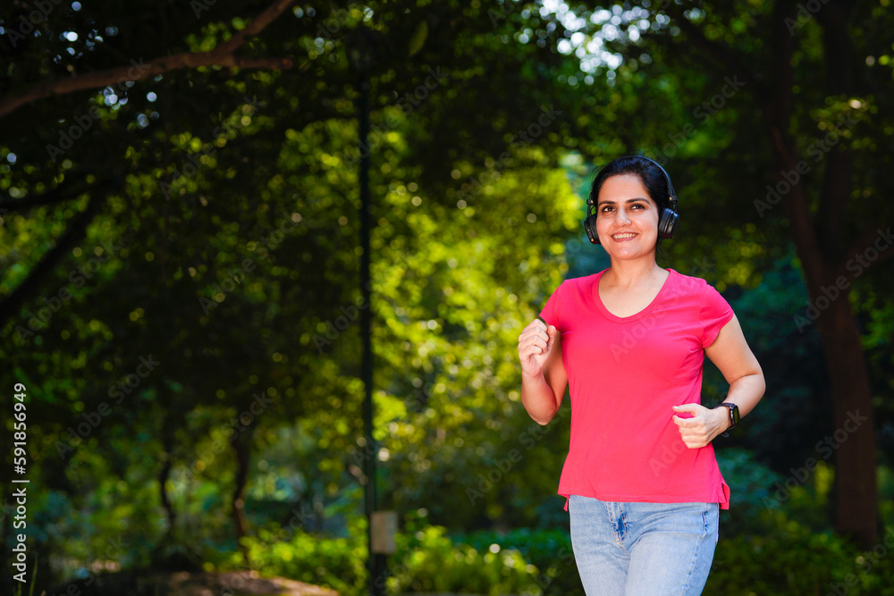 young indian woman with earphones listening music during jogging at park.