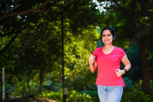 Fototapeta Naklejka Na Ścianę i Meble -  young indian woman with earphones listening music during jogging at park.