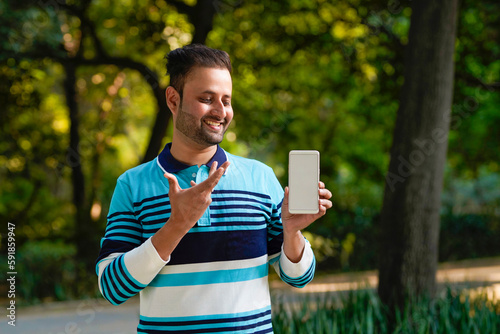 Indian man showing smartphone screen at park.