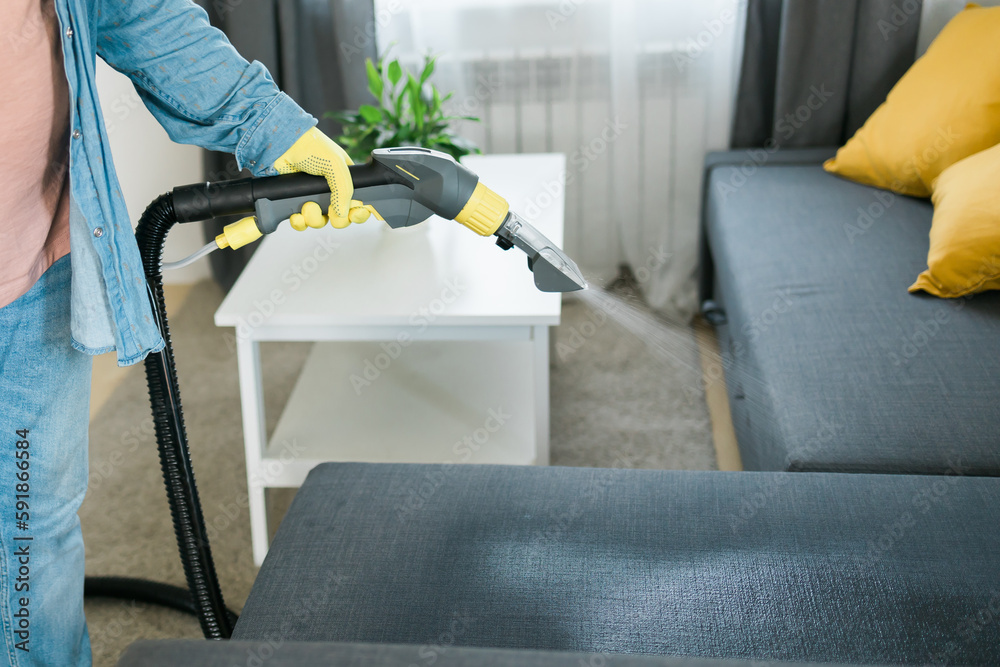 Cleaning service company employee removing dirt from furniture in flat with professional equipment. Man arm cleaning sofa with washing vacuum cleaner close up