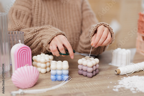woman making candles at home, close up of female hands cutting wick of bauble candle