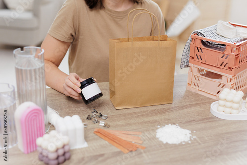 Woman packing homemade candle into paper bag photo