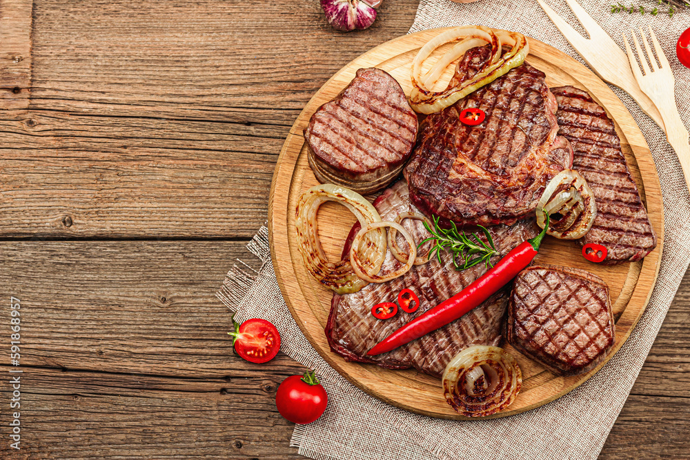 Grilled set of various steaks with vegetables. Ribeye, eye round, flank and striploin steaks Grilled set of various steaks with vegetables. Ribeye, eye round, flank and striploin steaks