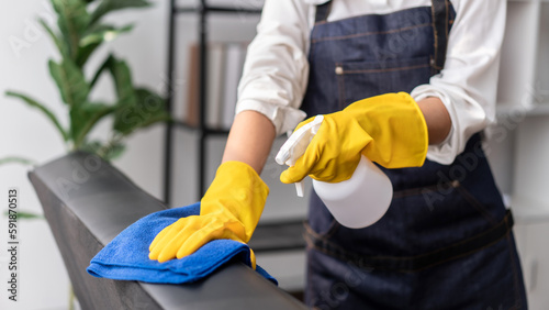 Housewife in apron wearing gloves to spraying hygiene spray on t