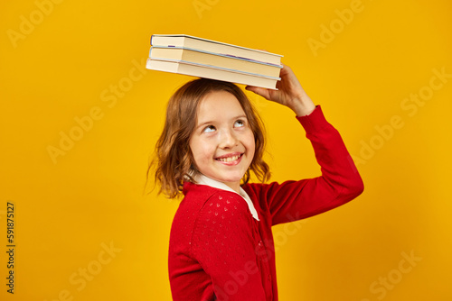 Portrait of happy teenage schoolgirl in uniform holding books on head