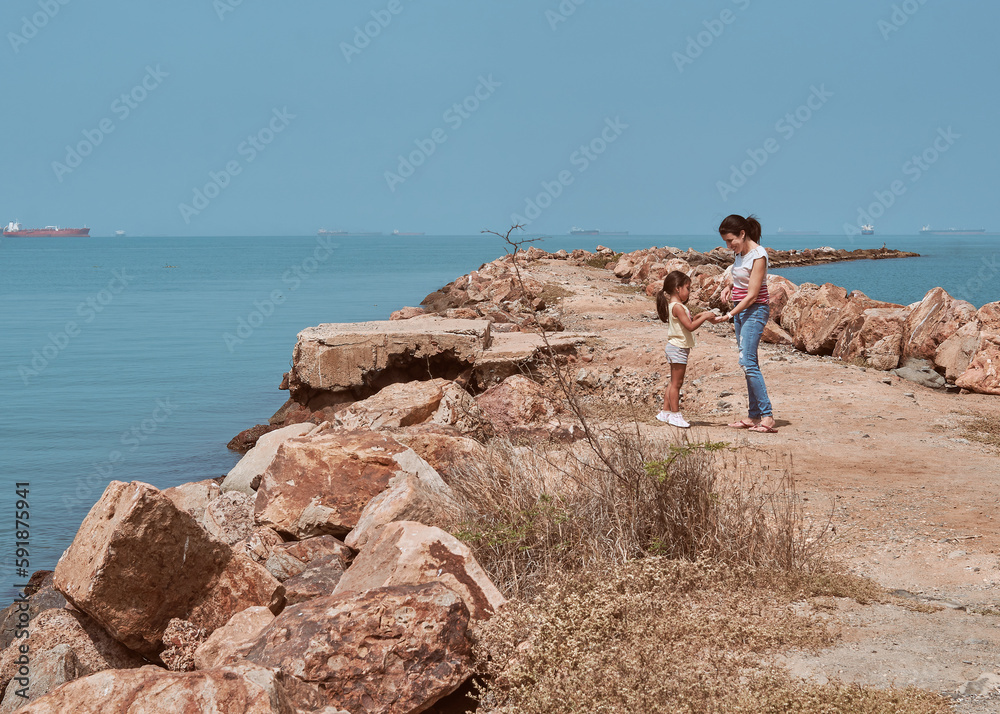 mother and daughter walking along wild roads, trails and the shores of a beach. Urban hikers walking along a mountain path along the shoreline of a beach, watching the sea, collecting rocks, interacti