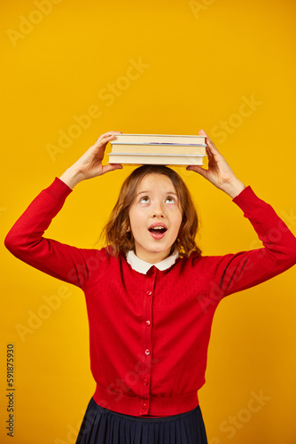 Portrait of happy teenage schoolgirl in uniform holding books on head