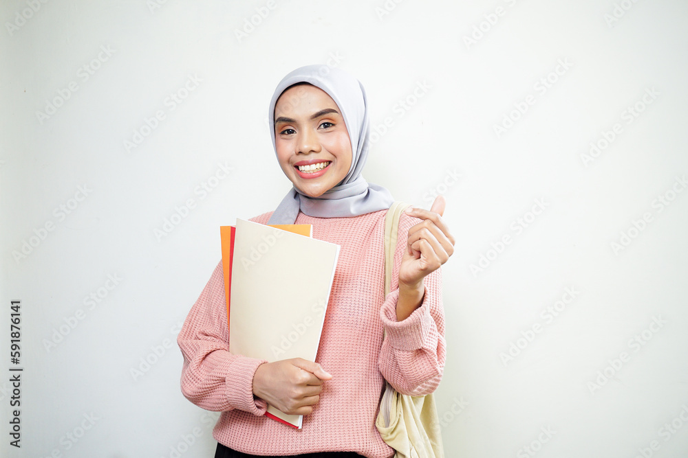 Excited young Asian Muslim woman student in pink sweater with bag, holding book isolated on white background. back to school concept Excited young Asian Muslim woman student in pink sweater with bag, holding book isolated on white background. back to school concept