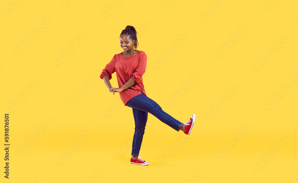 Cheerful young afro-american woman having fun isolated on bright yellow background. Smiling woman in casual clothes makes step and various movements looking down. Banner. Full length.