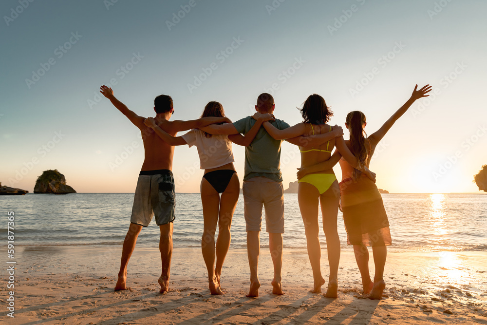 Fototapeta premium Five happy young friends are having fun and hugging at sunset sea beach