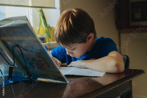 caucasian boy doing homework at home iat the table by the window. Image with selective focus photo