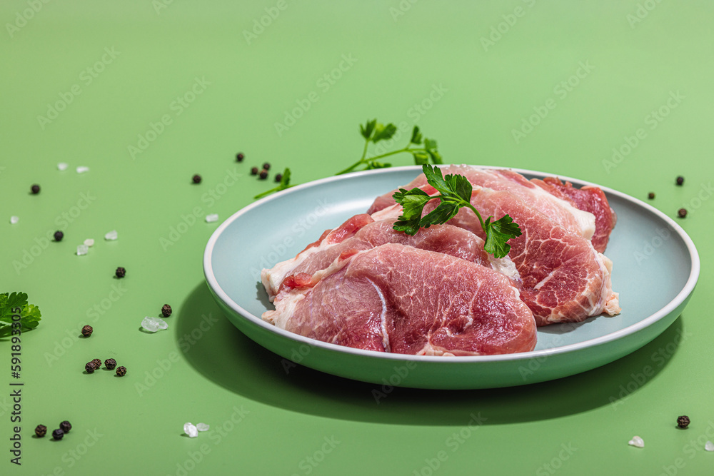 Pieces of pork meat with parsley on gray dish, raw fresh steaks concept. Sea salt, spices