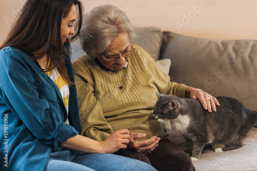 Grandmother and granddaughter petting a cat.